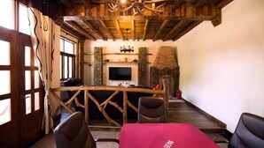 Een landelijk interieur met een stenen openhaard, houten balken en een aan de muur bevestigde televisie.