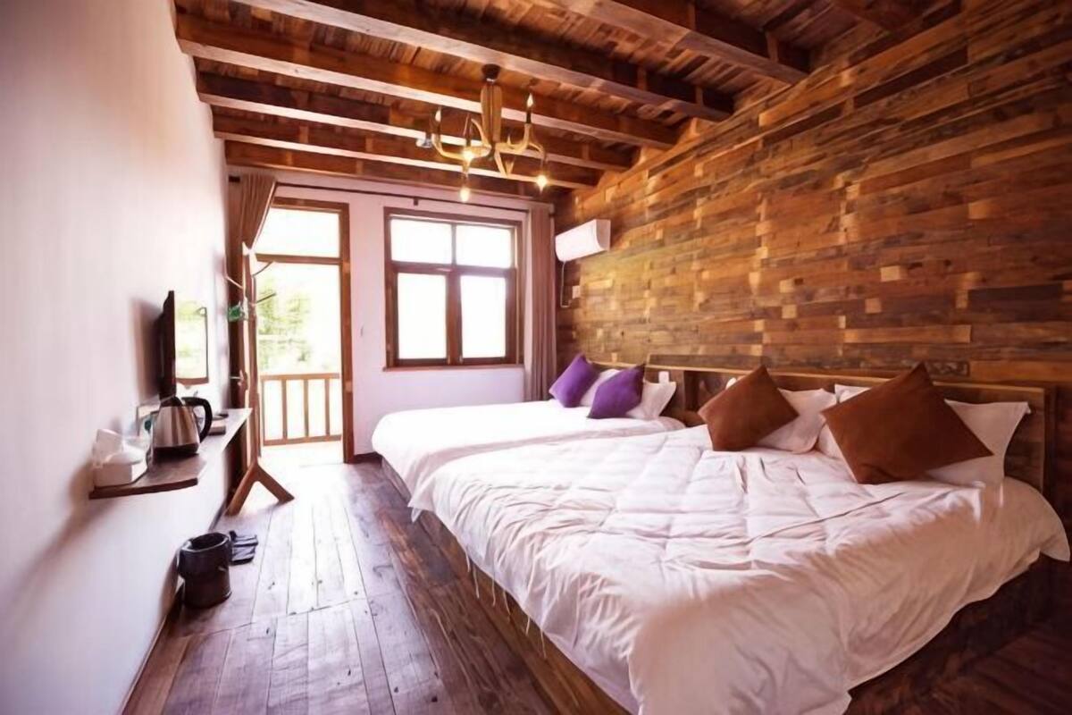 Una habitación con techo de madera, una cama con ropa blanca, un televisor sobre un mueble y una ventana con cortinas.