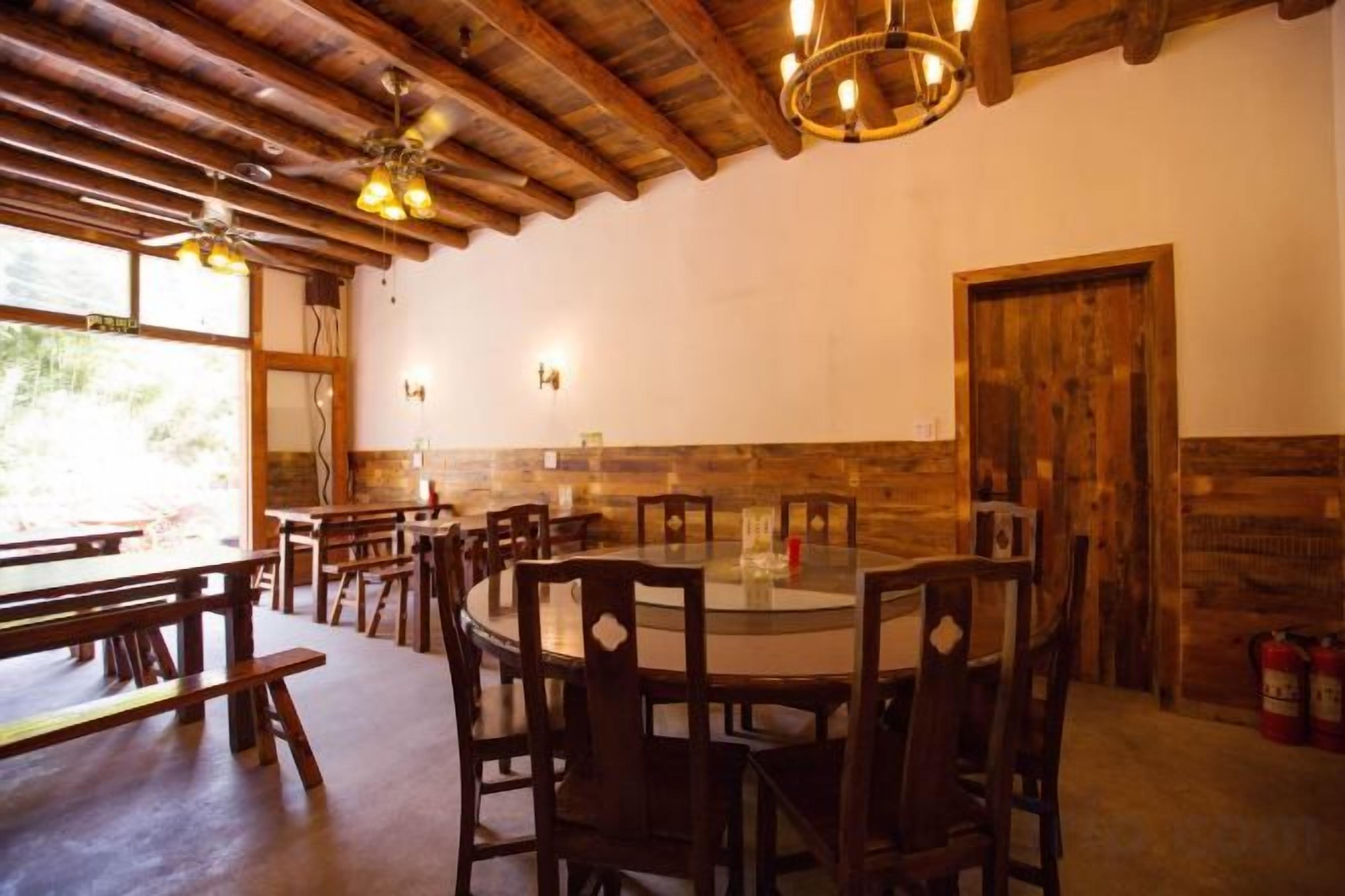A restaurant with wooden tables and chairs, a central round table, and a wooden ceiling.