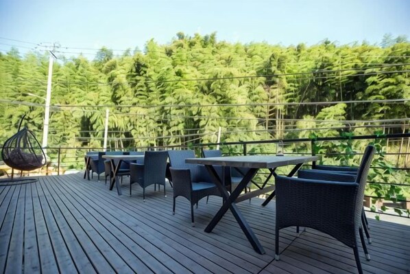 An outdoor deck with tables and chairs, surrounded by a forest.