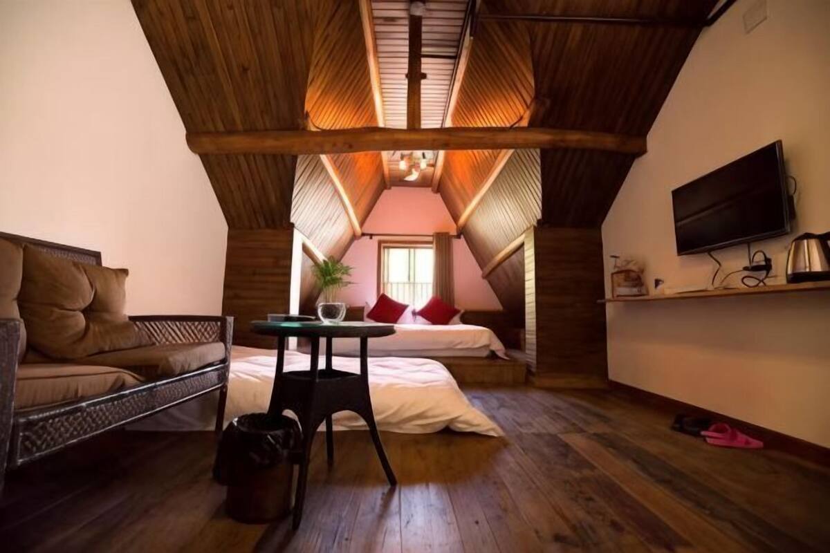 Un dormitorio acogedor en el ático, con cama, una mesita, televisor y ventana.