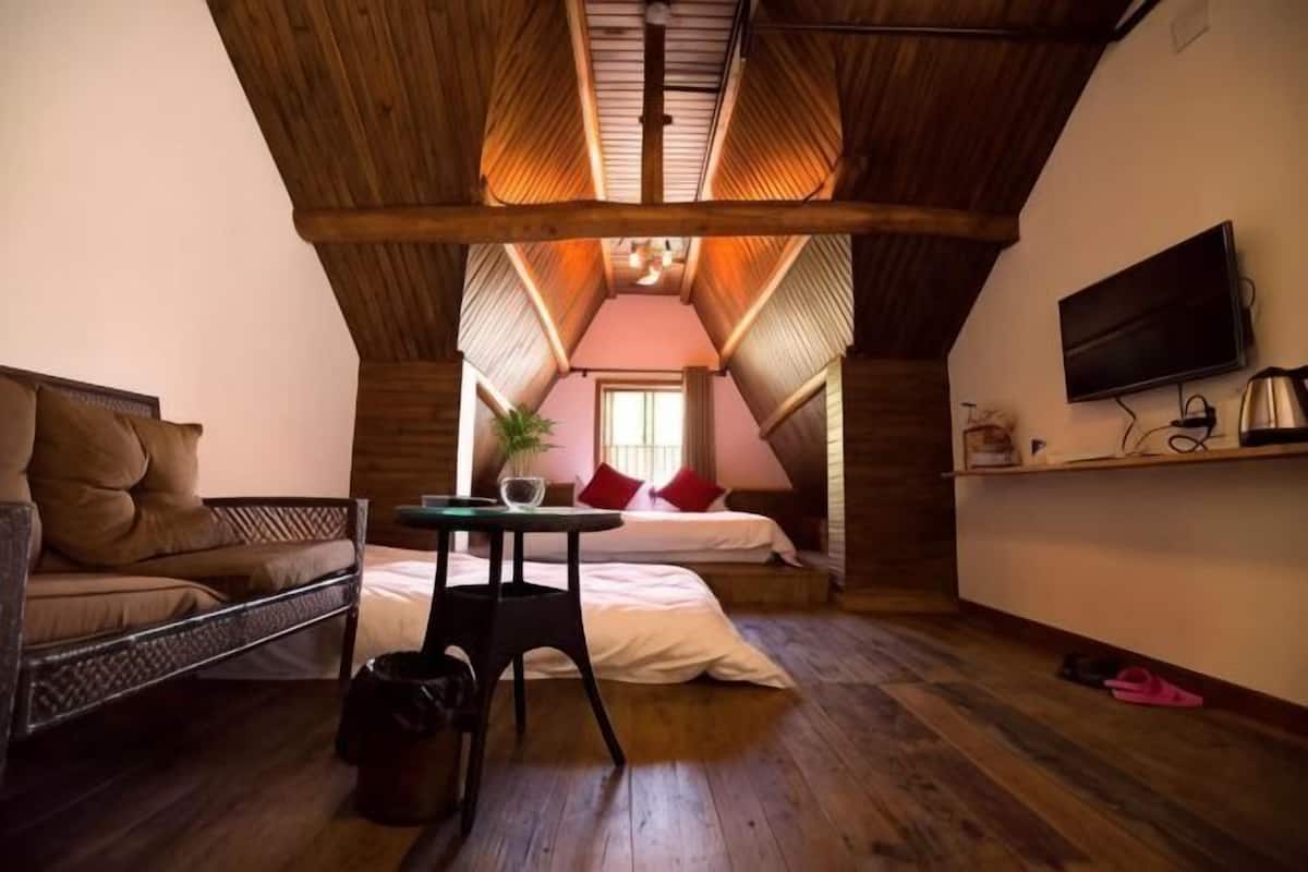 A cozy attic bedroom with a bed, a small table, a TV, and a window.