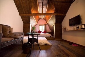 Un dormitorio acogedor en el ático, con cama, una mesita, televisor y ventana.