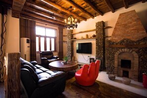 A cozy living room with a stone fireplace, leather sofa, red chair, and a flat-screen TV.