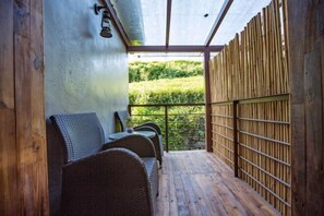 Un espace extérieur aménagé, abrité et doté de mobilier en osier, offrant une vue sur un paysage verdoyant.
