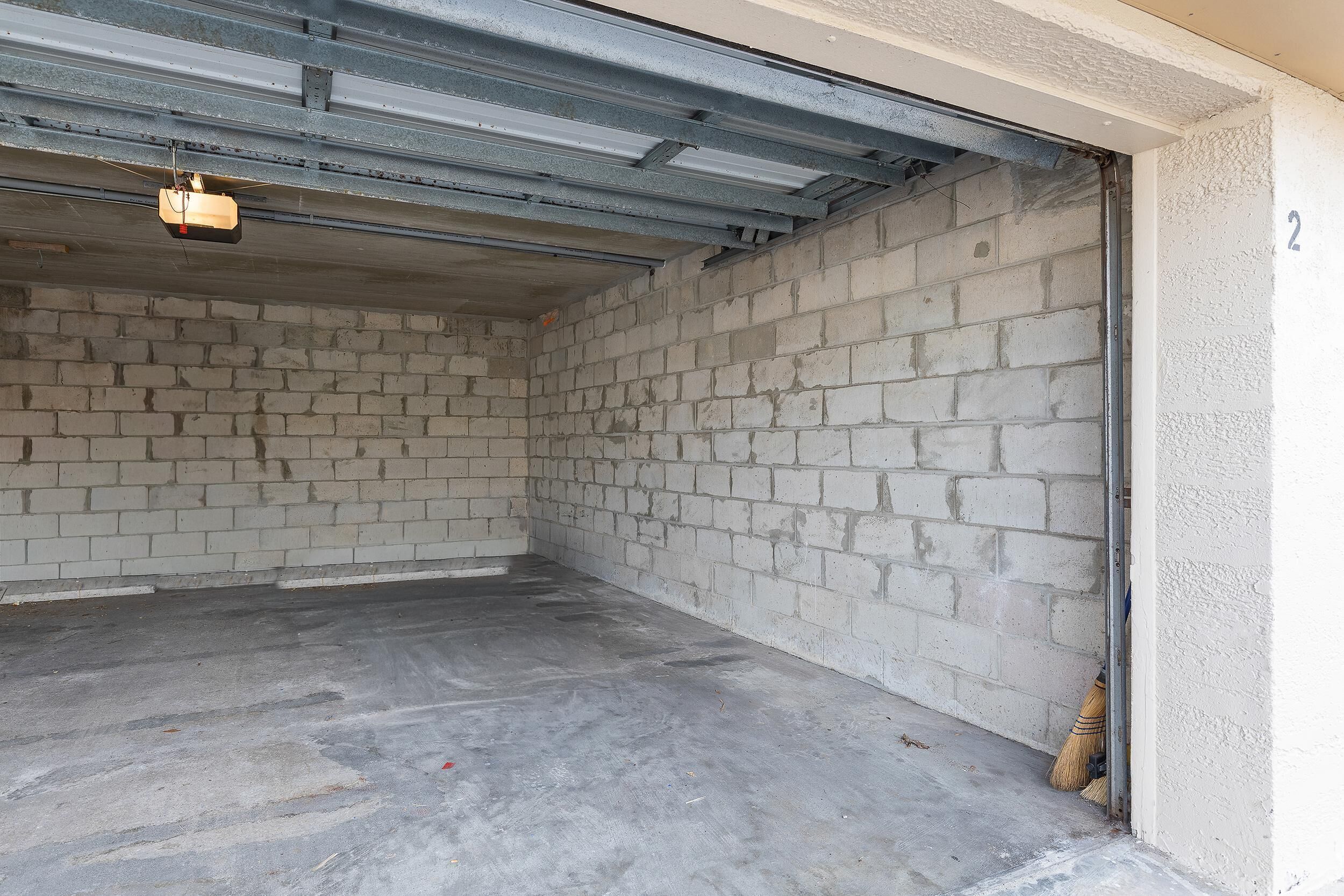 A garage with concrete walls and a metal roof, a broom leaning against the wall, and a number '2' on the right.