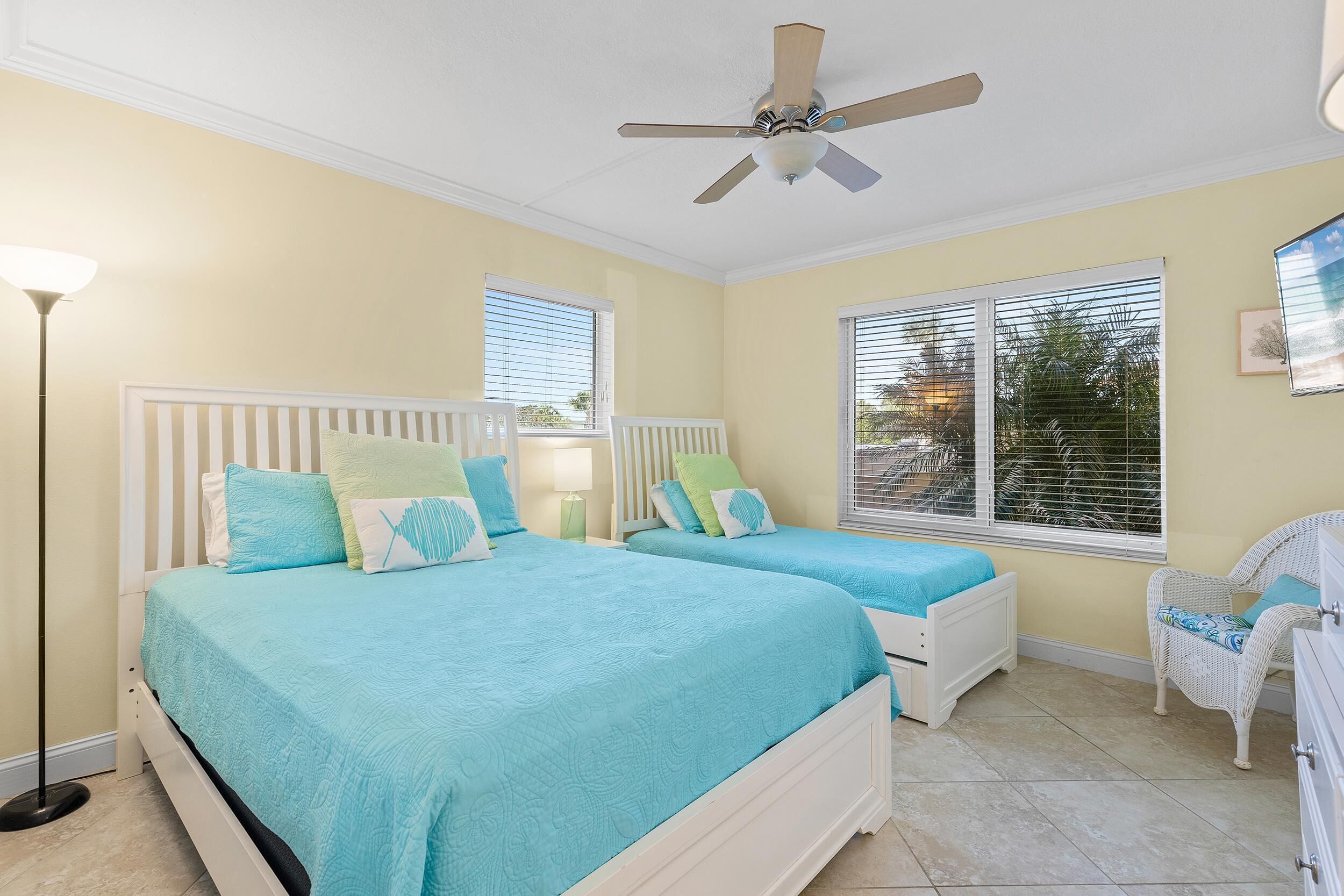A bedroom with two beds, a ceiling fan, and a window with blinds.
