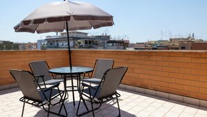 A rooftop terrace with a table and four chairs, an umbrella, and a view of surrounding buildings.