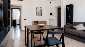 A modern living room with a dining area, a black bookshelf, and a large window.