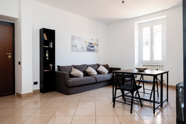 A modern living room with a sofa, a dining table, a bookshelf, and a painting on the wall.