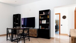 A modern living room with a flat-screen TV, a dining table with chairs, a black bookshelf, and a wooden cabinet.