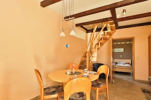 Zona pranzo con tavolo e sedie in legno, una scala e un letto sullo sfondo.