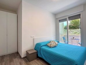 Une chambre à coucher comprenant un lit, un petit tabouret, une armoire et un balcon avec une table et des chaises.