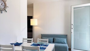 A modern room with a dining table, chairs, a sofa, a lamp, and a sliding glass door. - Dimora Venus - Comfort moderno sul mare (Fossacesia)