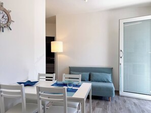 A modern room with a dining table, chairs, a sofa, a lamp, and a sliding glass door.