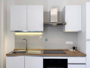 A modern kitchen with white cabinets, a stainless steel sink, a built-in oven, and a wooden countertop.