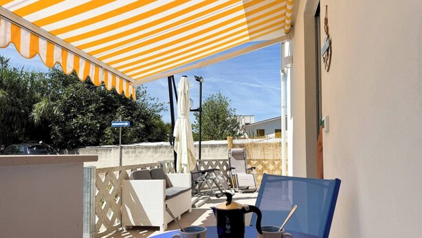 A balcony with a striped awning, a table with a coffee pot and cups, and outdoor furniture. - Dimora Venus - Comfort moderno sul mare (Fossacesia)