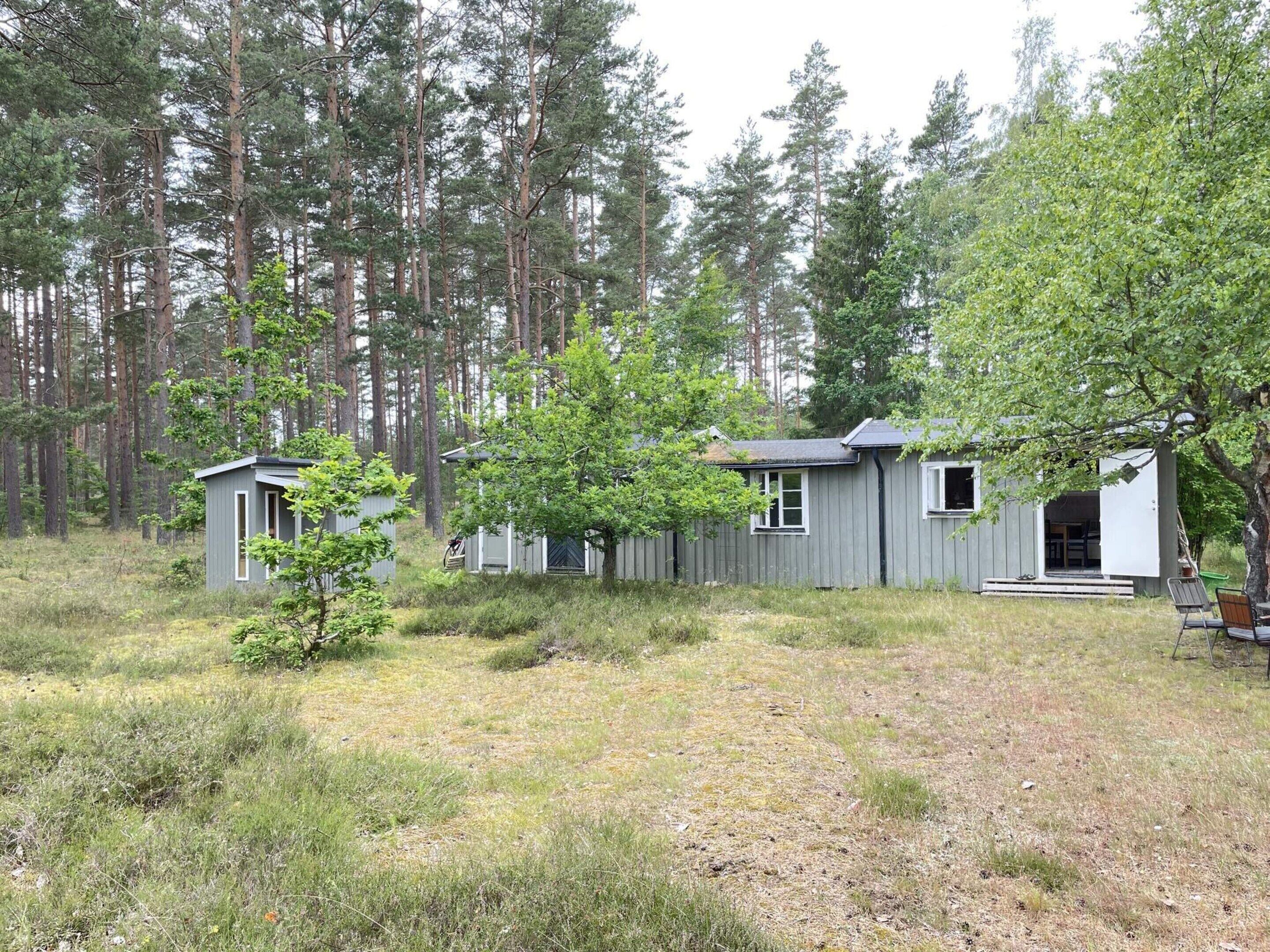 A cabin with a porch and a small deck, surrounded by a forest.