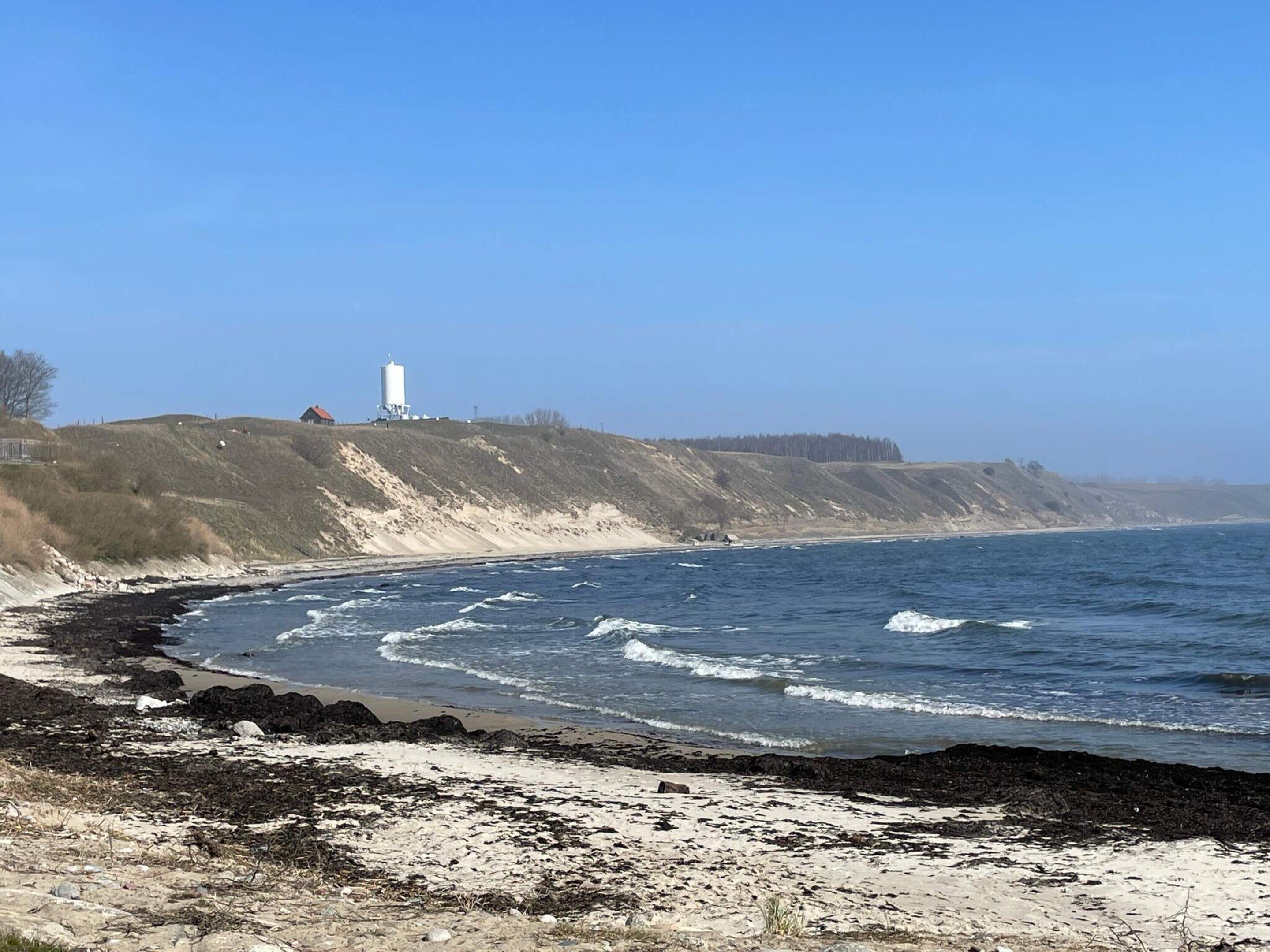 A coastal landscape with a lighthouse on a hill, a sandy beach, and rocky shoreline.
