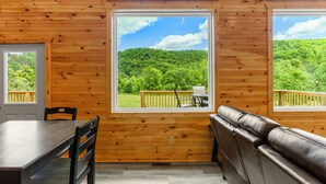 A wooden cabin interior with a dining table, chairs, and a leather bench. Large windows offer views of a forested area. - Trailer Parking/Hot Tub/King Size Beds/Mt Views (Stanton)