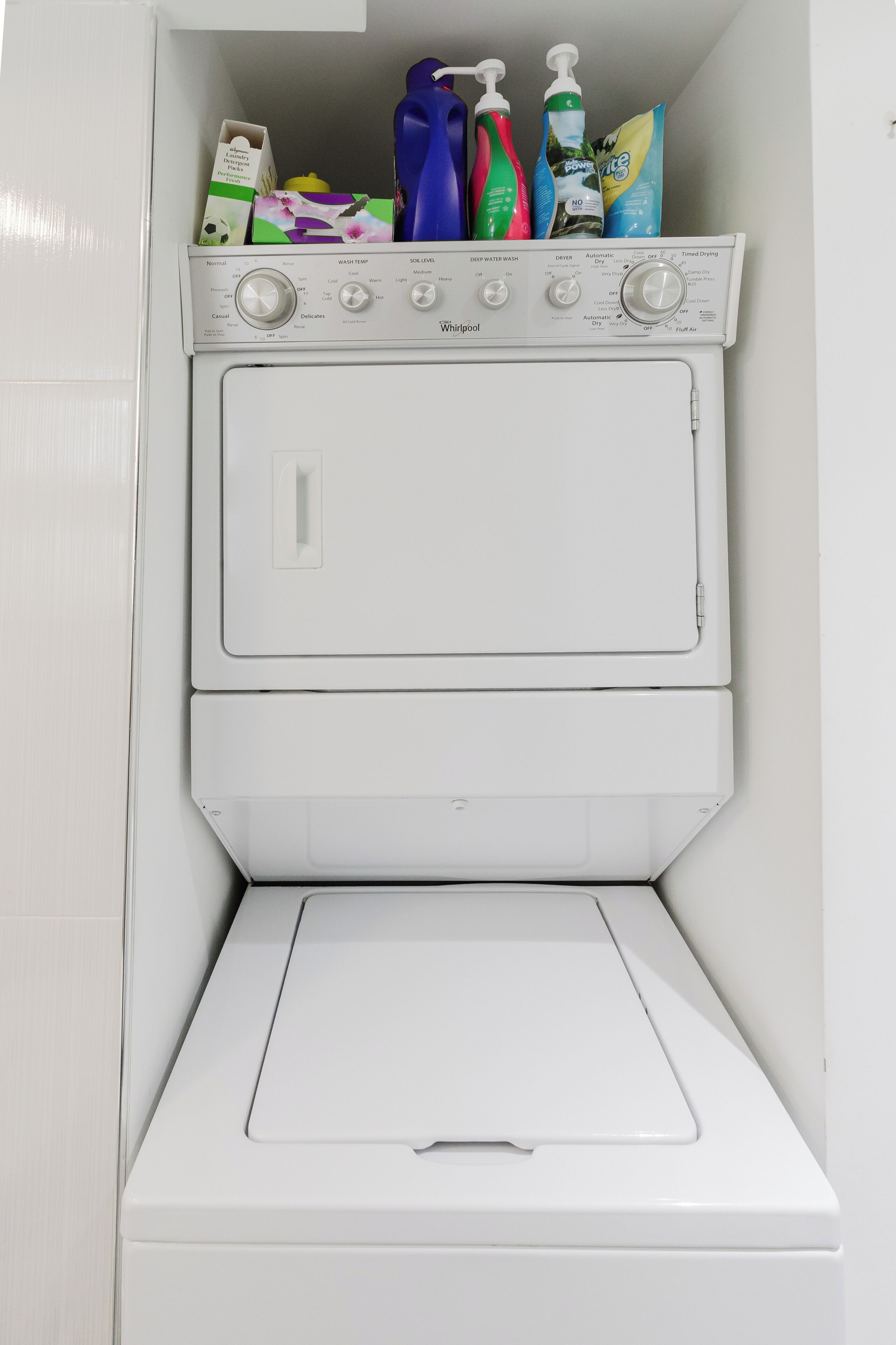 Una unidad de lavadora y secadora Whirlpool con botellas de detergente y una caja encima.