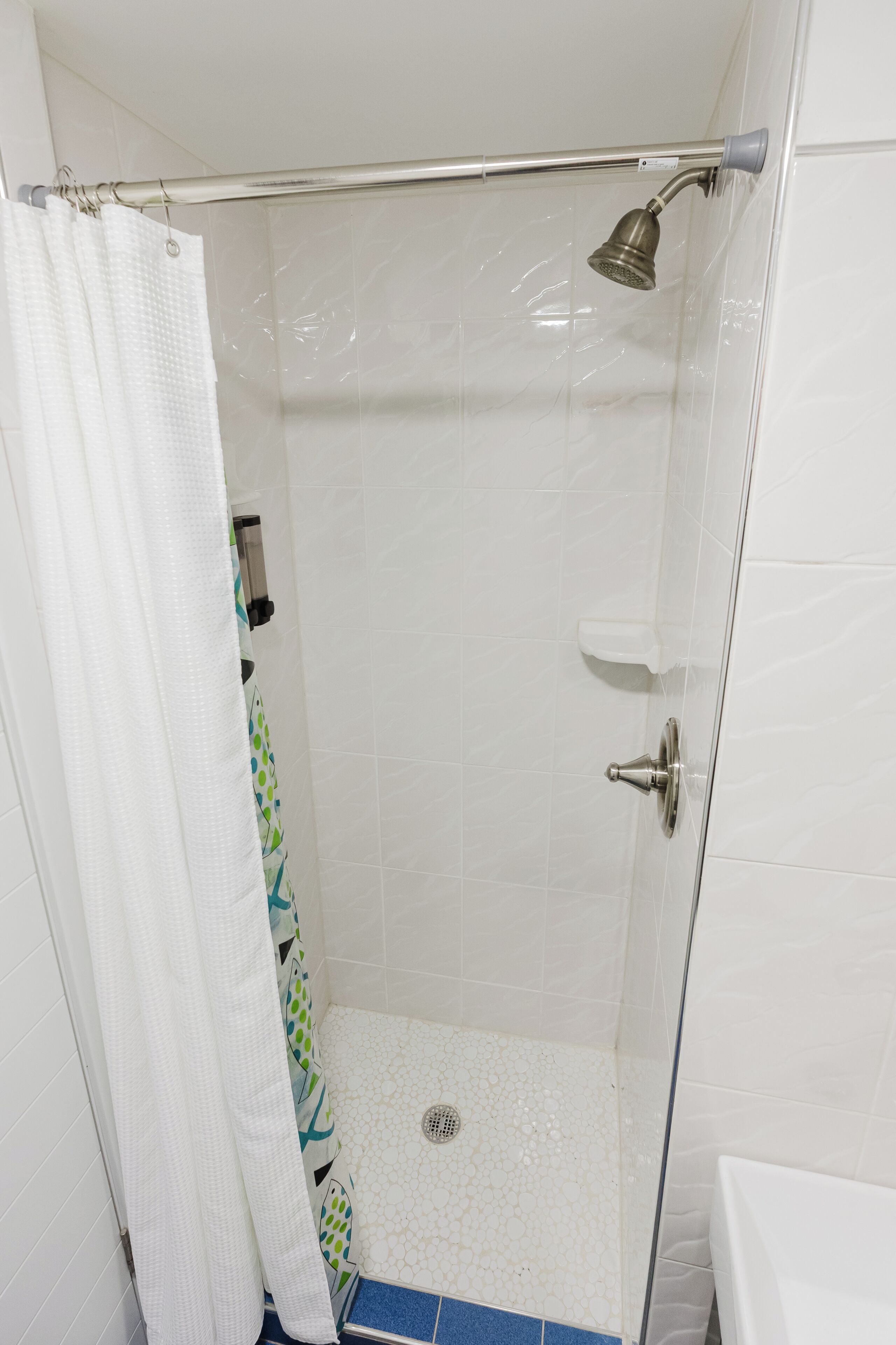 A shower with a glass door, a showerhead, a drain, and a white shower curtain.