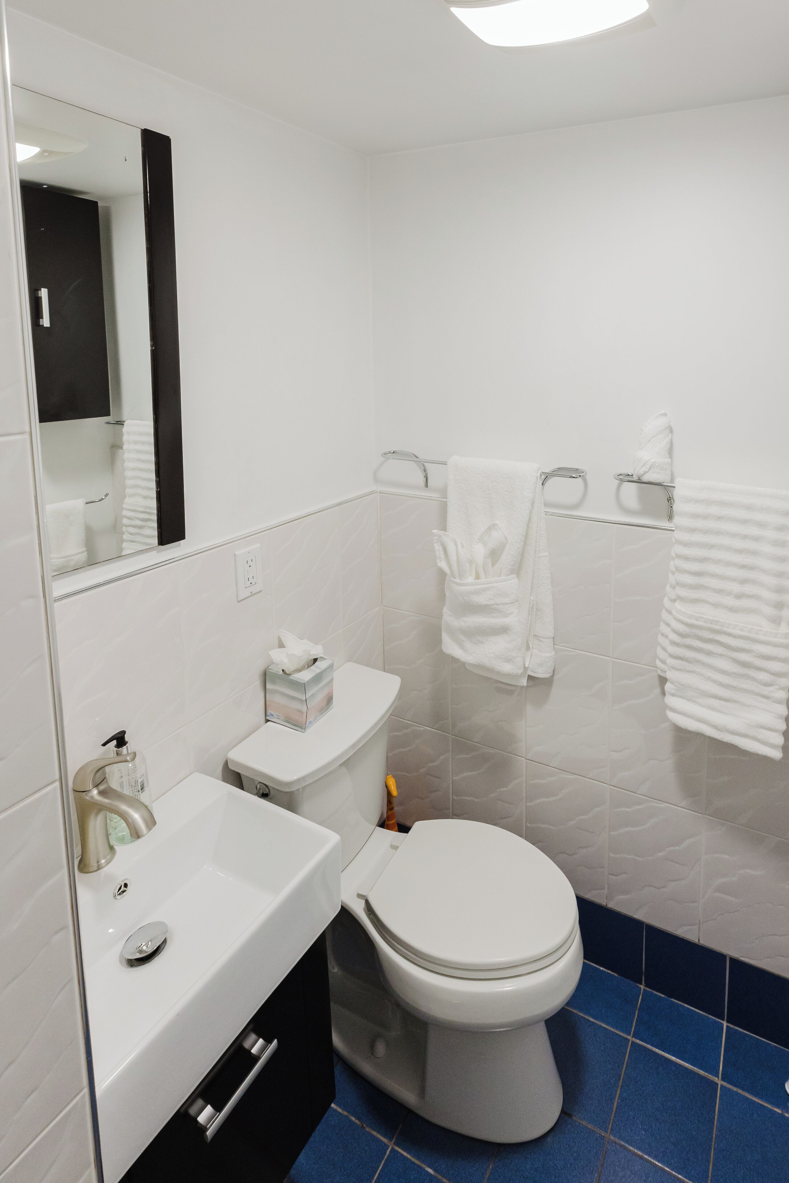 Un baño con lavamanos blanco, inodoro y suelo de baldosas azules.