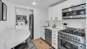 A modern kitchen with white cabinets, stainless steel appliances, and a marble countertop.