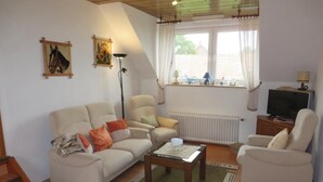 A living room with a sofa, armchairs, a coffee table, a floor lamp, and a TV. - NEW! Vacation apartment directly on the dike (Dornum)