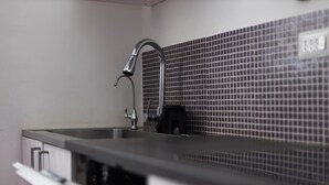 A kitchen with a stainless steel sink, a faucet, and a tiled backsplash. - Camera con bagno in centro città (Reggio Calabria)