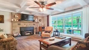 A spacious living room with a fireplace, comfortable seating, and large windows offering a view of the outdoors.