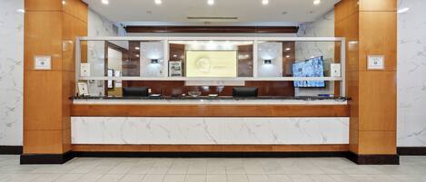 A reception desk with a marble counter, wooden paneling, and a security camera above.