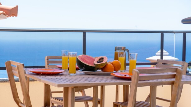 Ein Holztisch mit Tellern, Gläsern, einer Wassermelone und einem Saftkrug, mit Blick auf den Ozean.