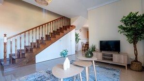 Ein modernes Wohnzimmer mit Holztreppe, Flachbildfernseher und einer großen Pflanze in einem Topf.