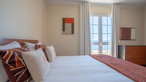 Ein Hotelzimmer mit einem großen Bett, einem Holzkopfende, Blick durch eine Glastür und einem gerahmten Kunstwerk an der Wand.