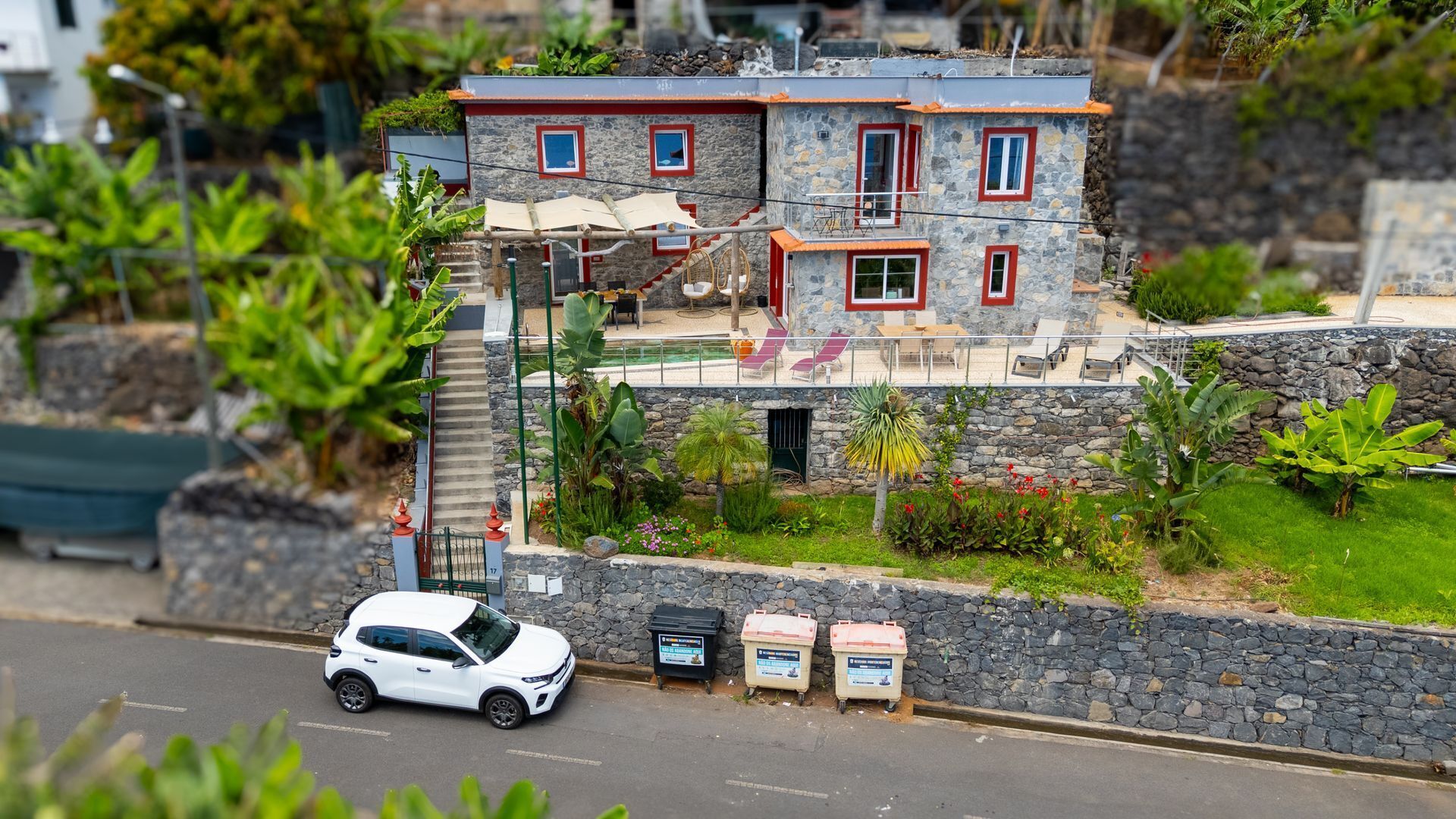 Un bâtiment en pierre de deux étages, avec un toit rouge, un escalier menant à l’étage supérieur et une petite voiture garée devant.