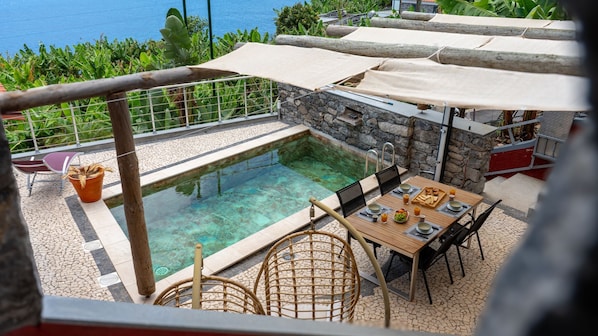 A poolside area with a table set for dining, surrounded by stone walls and a view of the sea.