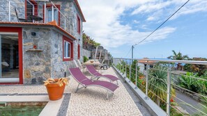 A stone building with a balcony, outdoor seating, and a view of the sea. - Fajã Stone House 1  by LovelyStay (Arco Da Calheta)