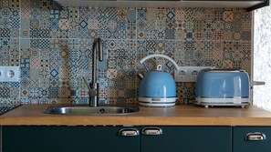 A kitchen with a tiled backsplash, a sink, a kettle, and a toaster. - Fajã Stone House 1  by LovelyStay (Arco Da Calheta)