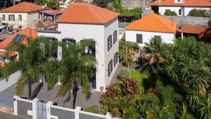 A white building with a red roof, surrounded by lush greenery and other buildings.