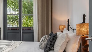 A hotel room with a bed, pillows, a lamp, a window with curtains, and a view of greenery outside. - Eden Funchal by LovelyStay (Funchal)