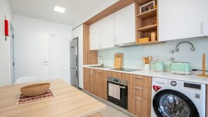 A modern kitchen with wooden cabinets, a built-in dishwasher, a washing machine, and a sink with a faucet. - Hygge Madeira by LovelyStay (Canico)