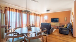 A modern living room with a round wooden table, leather sofas, and a flat-screen TV mounted on the wall. - BravaSol by LovelyStay (Tabua)
