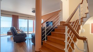 A spacious living area with a wooden staircase, a balcony with a view, and a leather sofa. - BravaSol by LovelyStay (Tabua)
