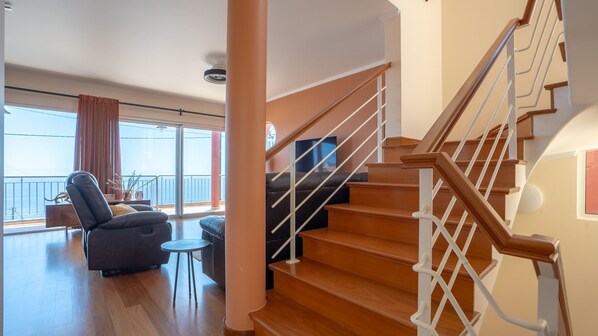 A spacious living area with a wooden staircase, a balcony with a view, and a leather sofa.