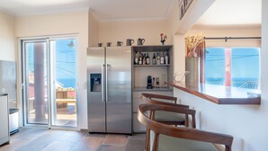 A modern kitchen with a stainless steel refrigerator, a wine rack, and a dining area with wooden chairs. - BravaSol by LovelyStay (Tabua)