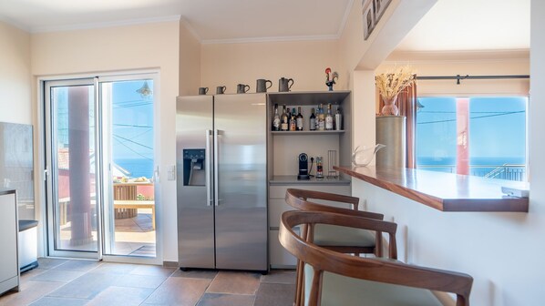 A modern kitchen with a stainless steel refrigerator, a wine rack, and a dining area with wooden chairs.
