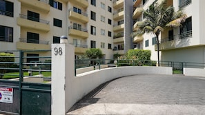A multi-story residential building with balconies, a gated entrance, and a paved driveway.