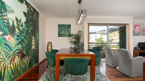 Un salon moderne avec un coin repas, de grandes fenêtres et des œuvres d’art sur le thème des tropiques.
