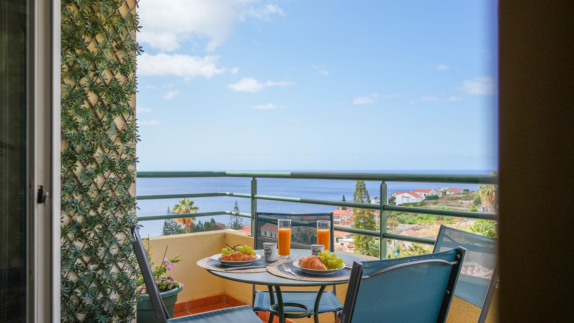 A balcony with a table set for breakfast, overlooking a coastal view.